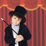 Adorable child dress of illusionist with hat and red curtains of background