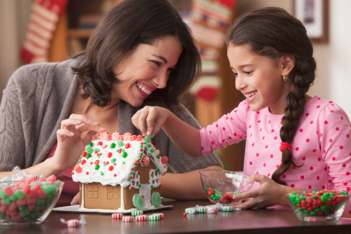 An image of a mother and daughter decorating a gingerbread house as a christmas activity 
