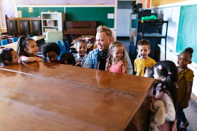 Preschool teacher surrounded by his students playing piano