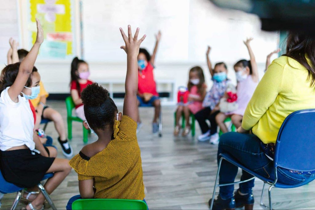 Image of kids sitting in class and raising hands