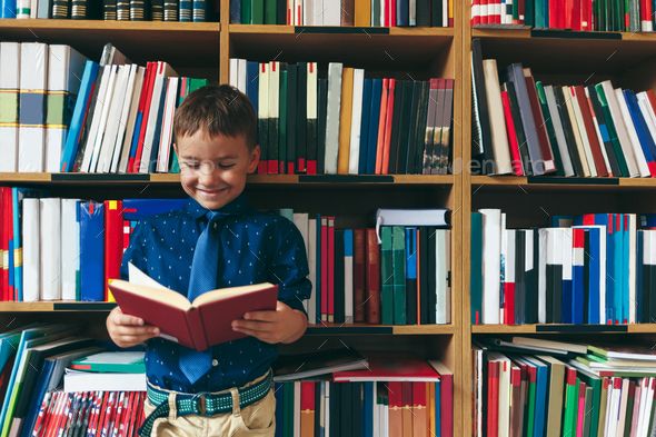 Little smiling child reading a opened book in library Little child smiling reading a book in library