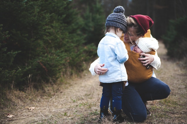 woman with brown baby carrier and little kid in white jacket parallel parenting woman with brown baby carrier and little kid in white jacket parallel parenting