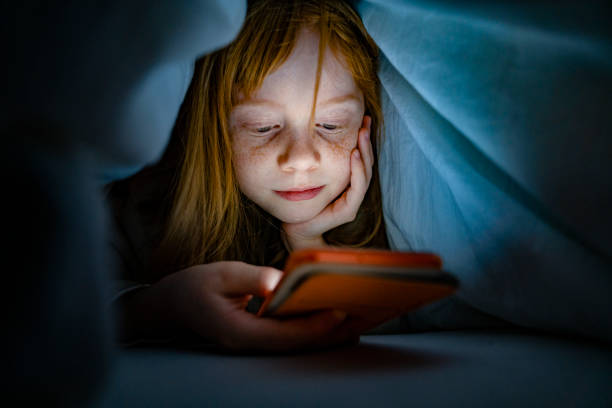 Image of a kid using phone at night under the blanket 