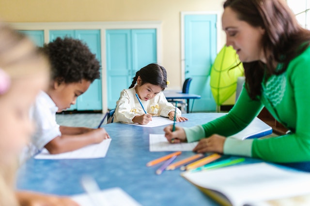 woman in green long sleeves teaching kids in daycare woman in green long sleeves teaching kids in daycare