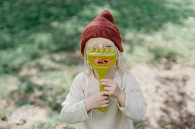 Cute little girl holding toy rake near face in garden Charades for kids