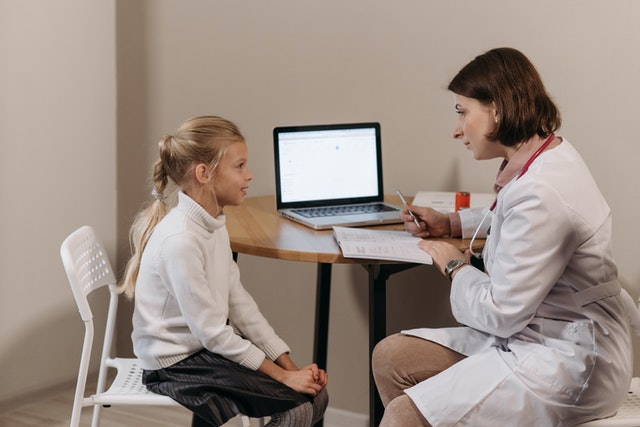 Doctor in white lab coat sitting in front of little girl and listening developmental disabilities