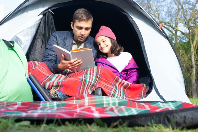 Father and daughter reading a book while sitting inside the tent Kids camping