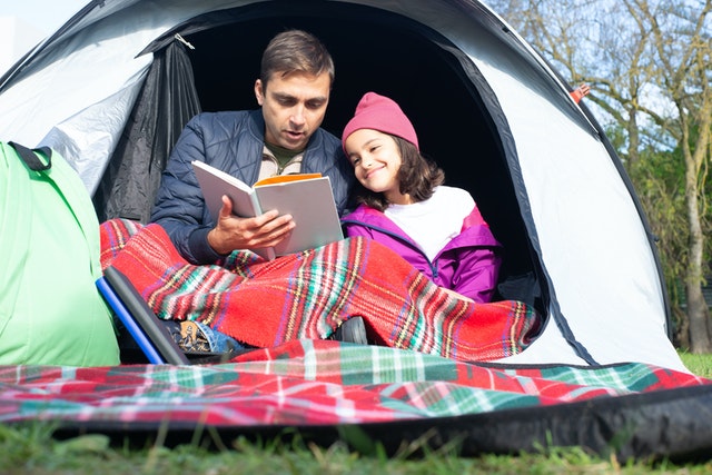 Father and daughter reading a book while sitting inside the tent Kids camping Father and daughter reading a book while sitting inside the tent Kids camping