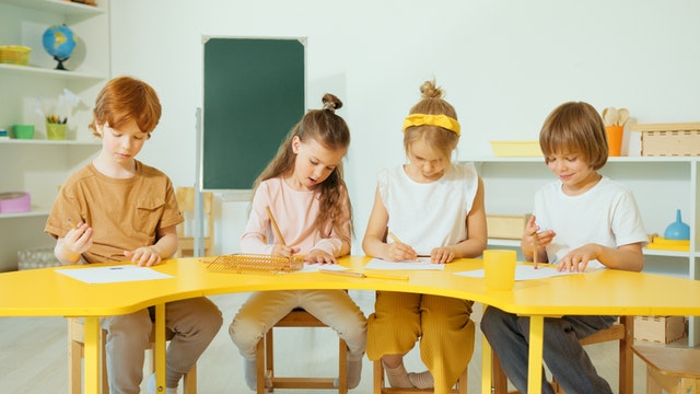 Kids sitting on yellow table writing and reading