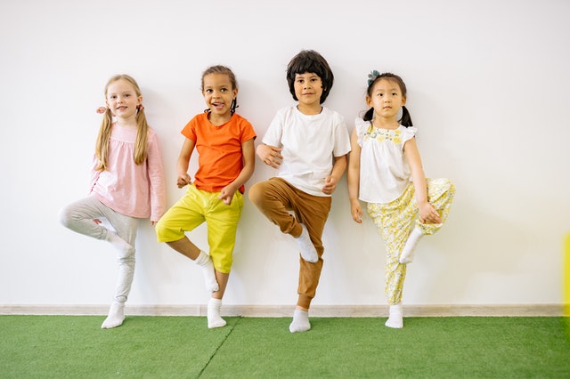 Kids standing and balancing on one foot on a green carpet workouts for kids