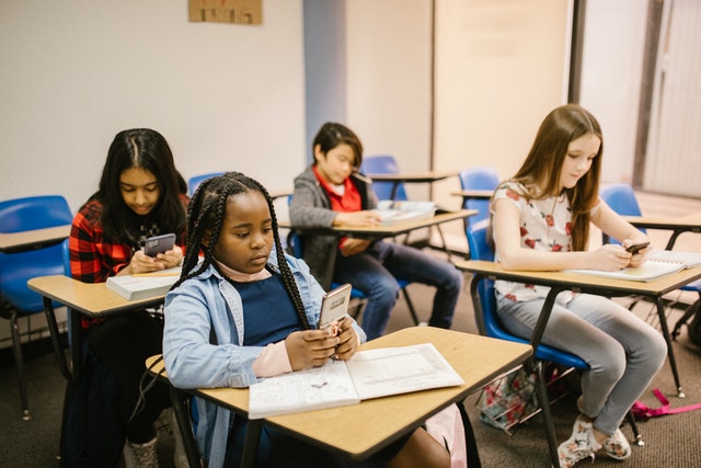 Students sitting in classroom using smartphone Classroom Organization Ideas