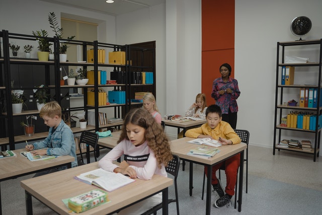 Students sitting on chair teacher standing in back Classroom Organization Ideas