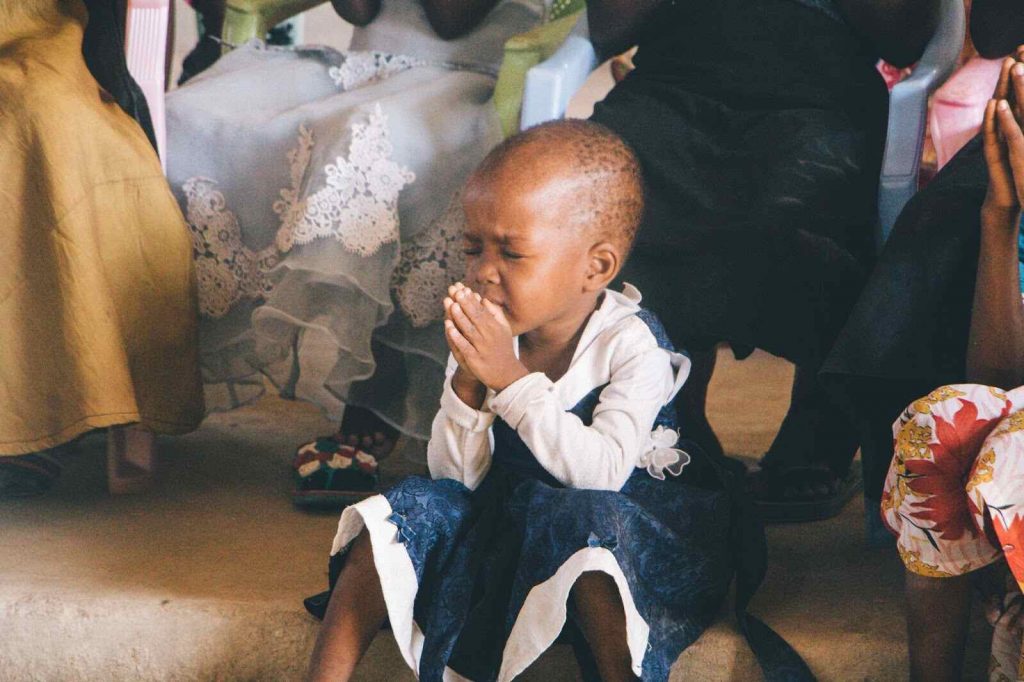 Young girl praying with folded hand sitting on ground prayers for children