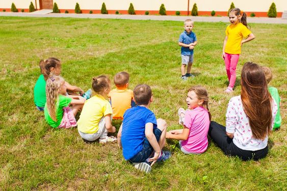 children sitting in grass field park charades for kids