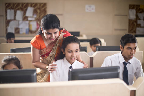 Image of kids in computer class with teacher assisting them
