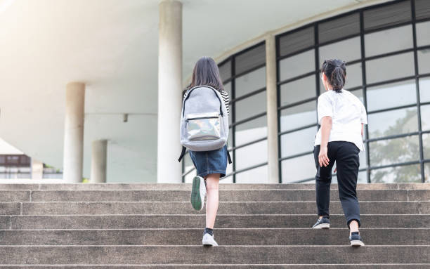 Back to school education concept with girl kids elementary students carrying backpacks going running to class on school first day and walking up building stair happily