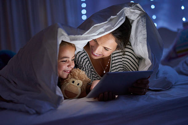 Shot of a mother using a digital tablet with her daughter under a blanket fort