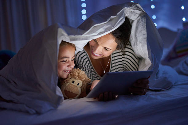 Shot of a mother using a digital tablet with her daughter under a blanket fort Shot of a mother using a digital tablet with her daughter under a blanket fort