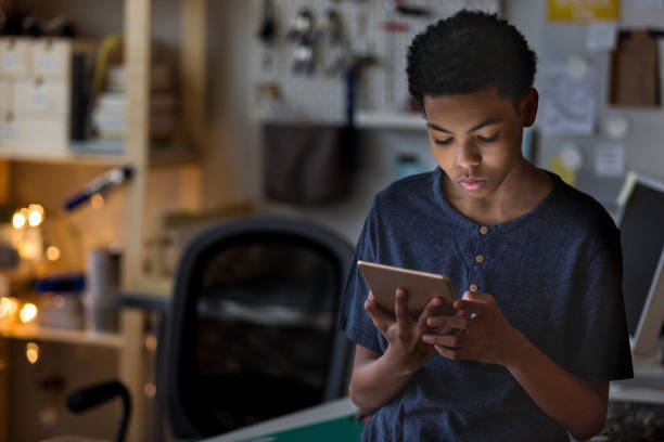 A teen boy plays a game in his room on a digital tablet at night A teen boy plays a game in his room on a digital tablet at night