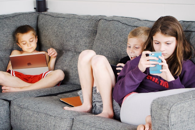 Children lying on sofa and using gadget reading apps