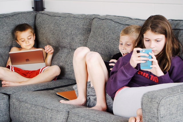 Children lying on sofa and using gadget reading apps Children lying on sofa and using gadget reading apps