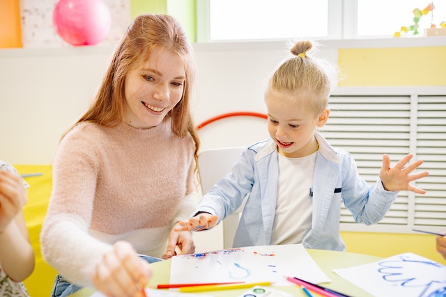 Girl learning to paint with her teacher What is taught to kids in kindergarten Girl learning to paint with her teacher What is taught to kids in kindergarten