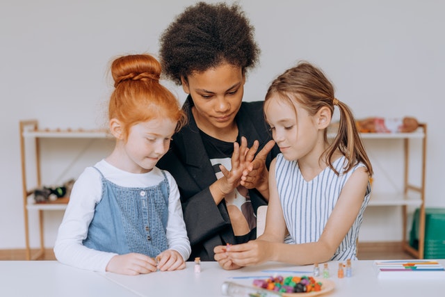 Girls sitting beside a woman in black blazer What is taught to kids in 3rd grade