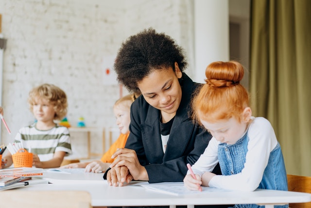 Teacher helping young girl with writing in class