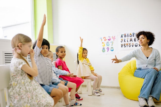 Teacher giving lesson and children raising their hands