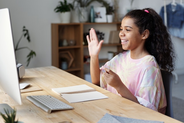 Girl in pink shirt sitting on the table waving on video call
