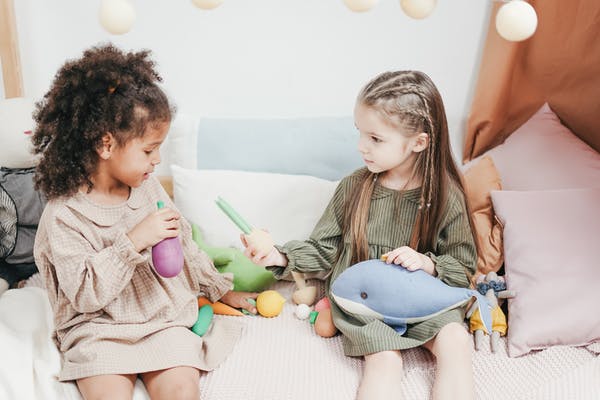 Two young girls sitting on a sofa playing with each other