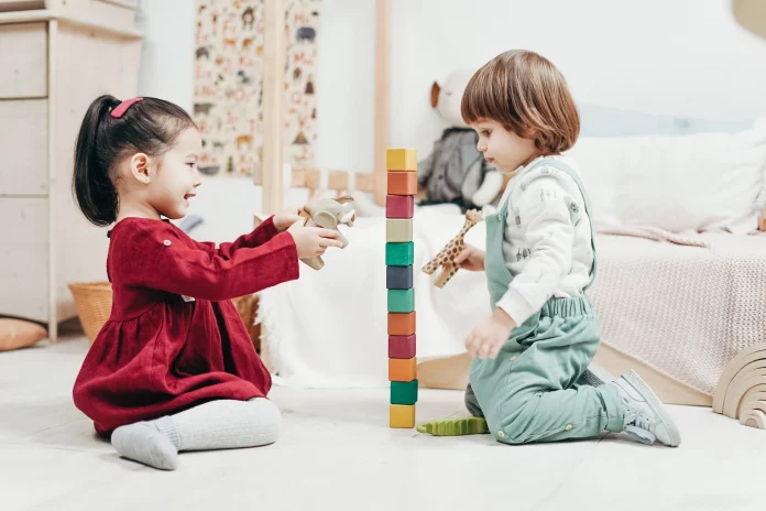 Boy sitting on the floor beside girl playing with blocks
