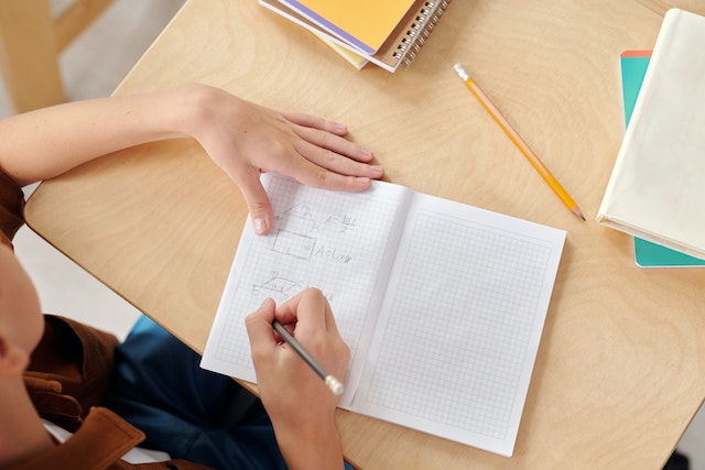 Young kid drawing geometrical shapes in a notebook with a pencil