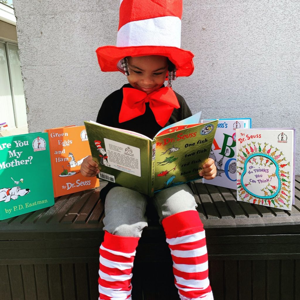 Young boy sitting outdoors surrounded by picture books reading Dr Seusss One Fish Two Fish Red Fish Blue Fish