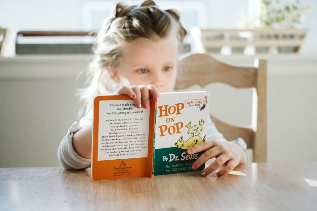 Young girl sitting at table and reading the book Hop on Pop by Dr Seuss