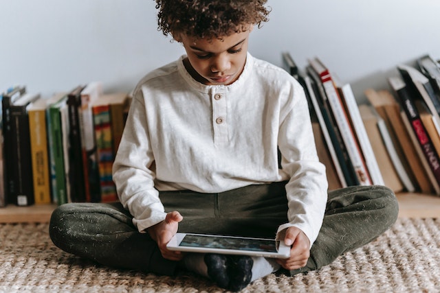 Young boy sitting on rug, looking at a tablet
