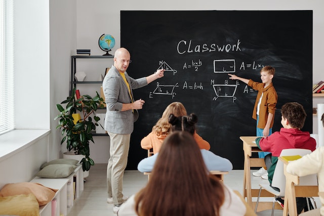 howcaniimplementmentalmathinmyclassroom Teacher pointing to geometric figures on a blackboard in a classroom full of students