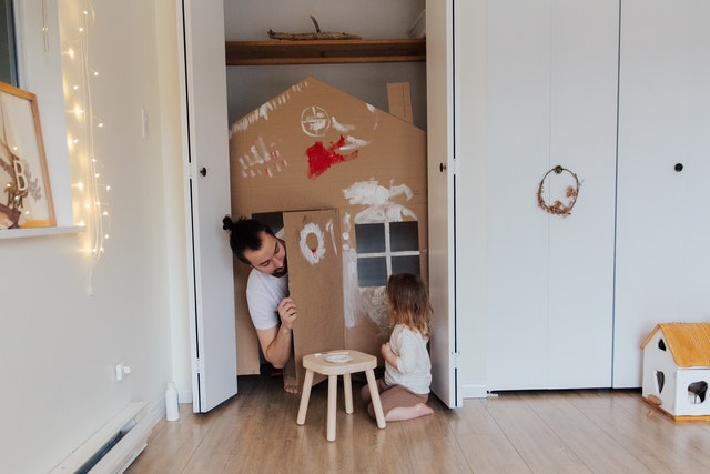 man playing with daughter in a cardboard home