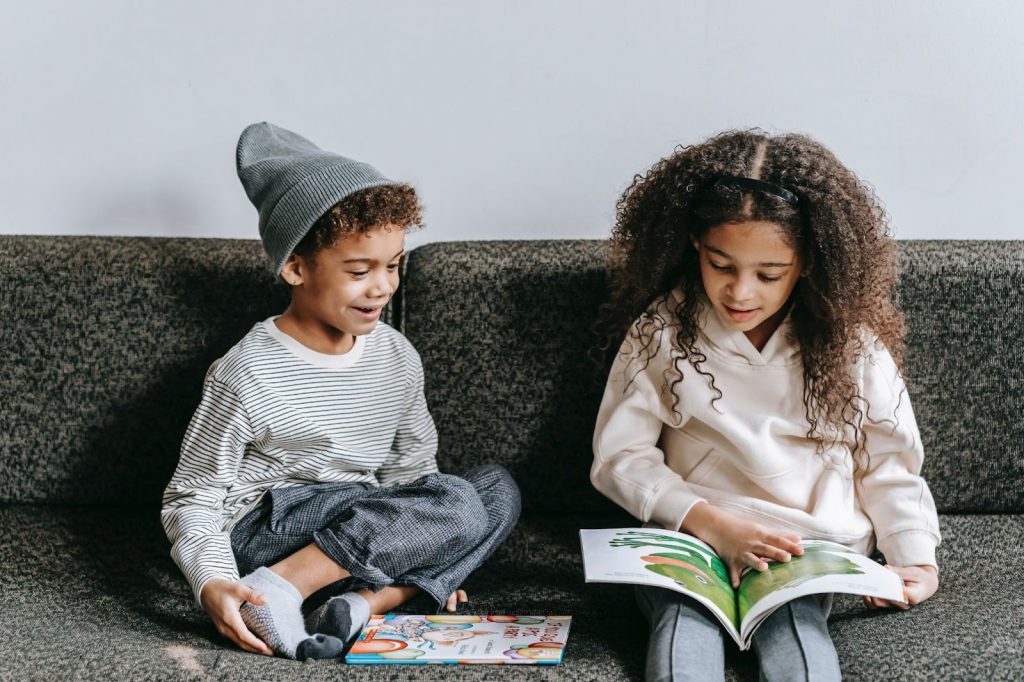 Two kids reading picture books while sitting on a couch