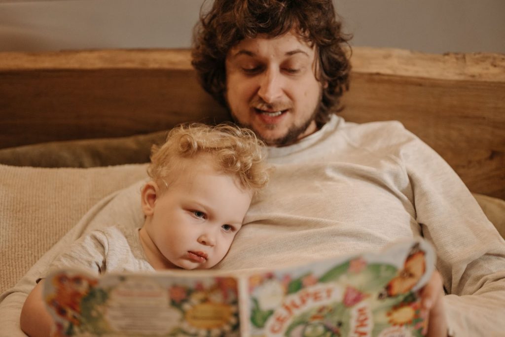A parent with a child, reading a book in bed
