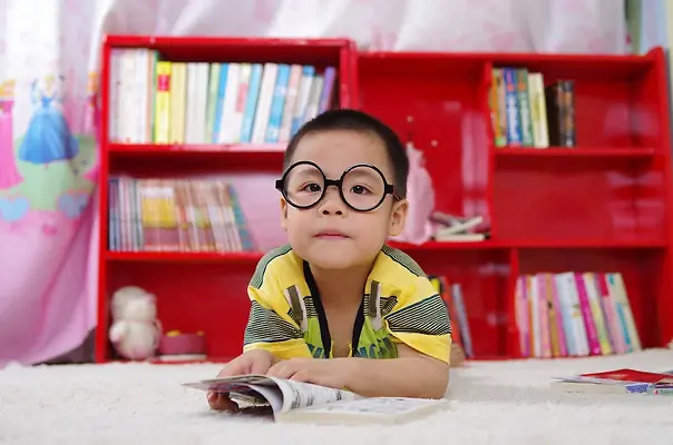 Young boy with glasses reading book in library