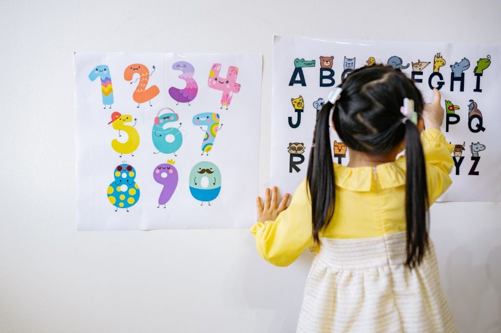 Young girl reading letters on a poster stuck to a wall