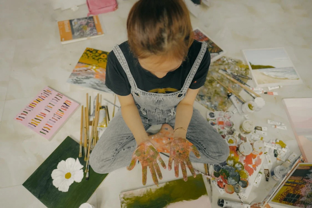 Small girl with hands filled with paint sitting on floor