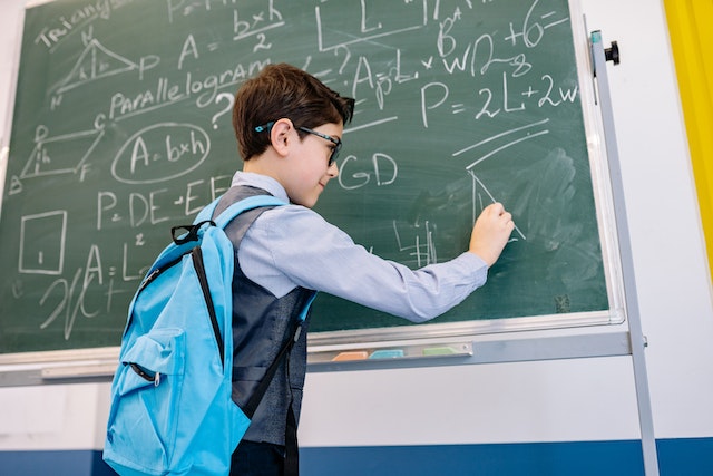 Young boy writing math equations on a blackboard with chalk