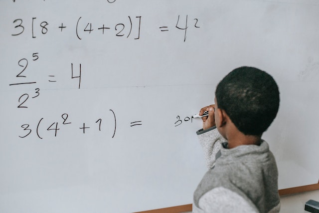 Young boy writing a math equation on a whiteboard