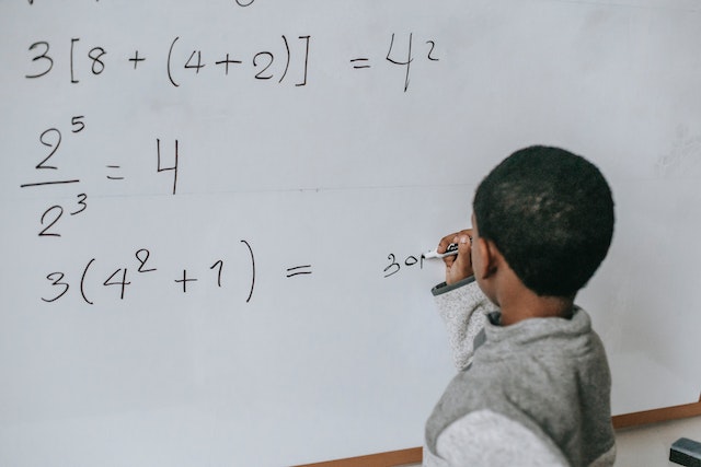 whyarementalcalculationsimportantforkids Young boy writing a math equation on a whiteboard