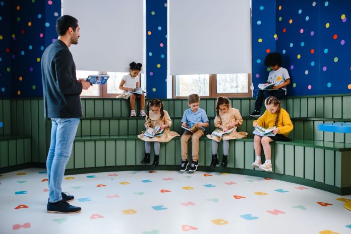 Children looking at their books in a classroom while a teacher teaches