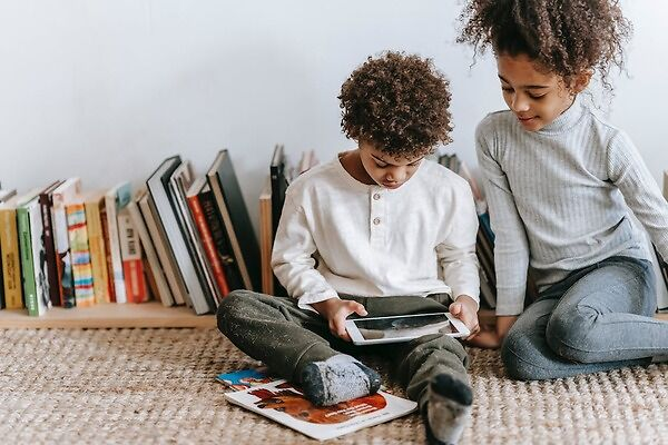 Young boy and girl sitting on a rug looking a tablet