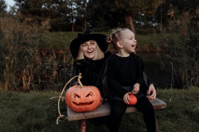 Mother and daughter in Halloween costumes share a park bench
