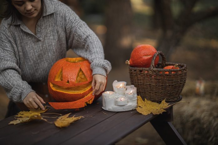 A woman carves a pumpkin into a jack o’ lantern on a wooden table